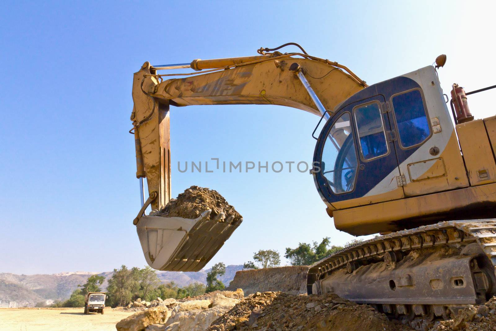 The back hoe is lifting and moving dirt.Back hoe vehicle on a pile of dirt