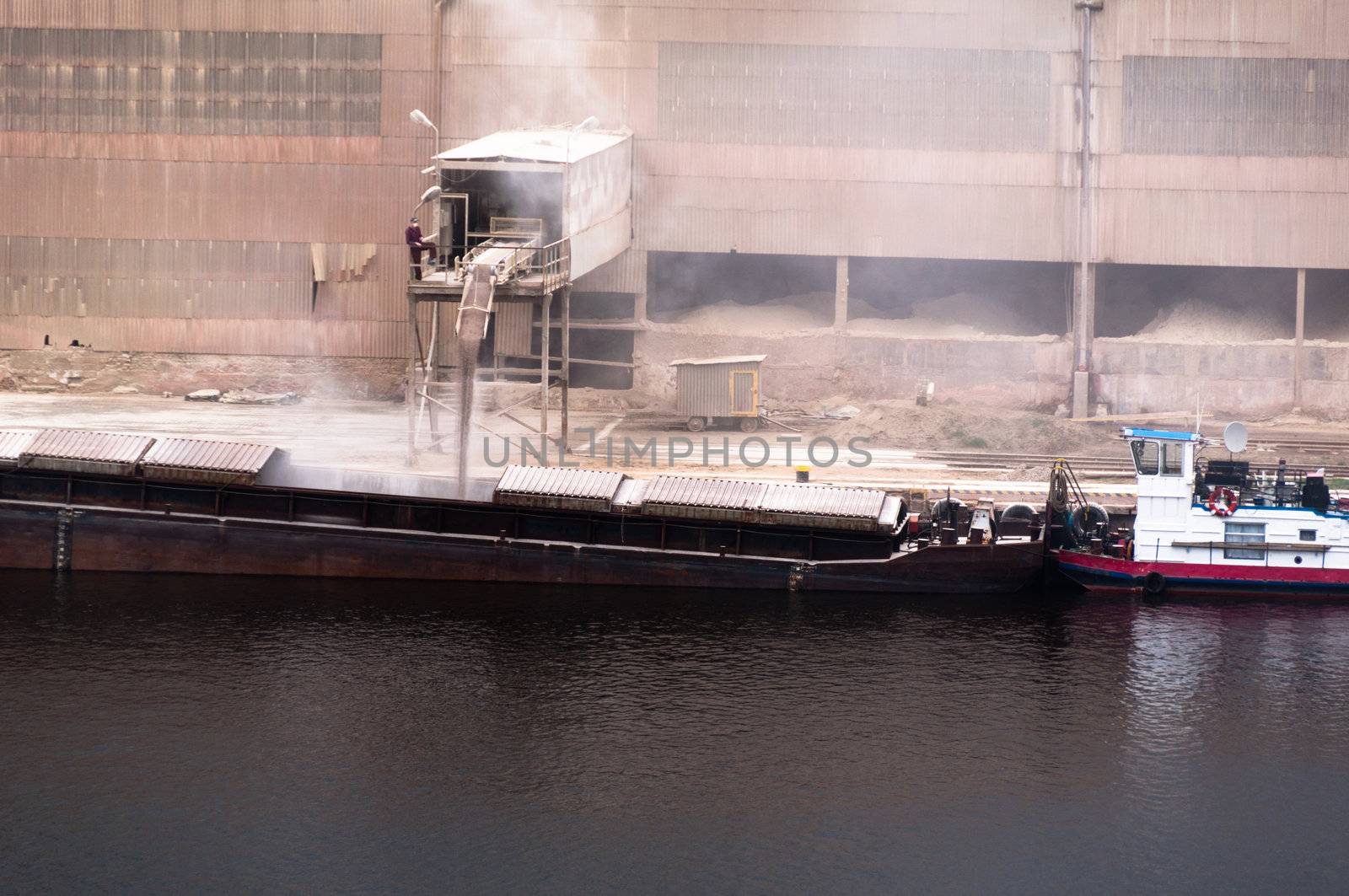 A transport ship is being loaded with powder/grain the oldfashioned way with dust all over