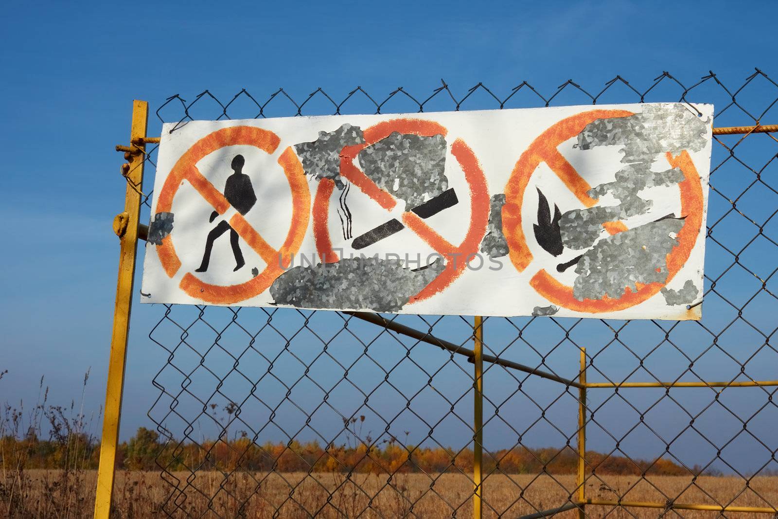 Old table with prohibitive signs and shelled paint hanging on mesh fences in fields