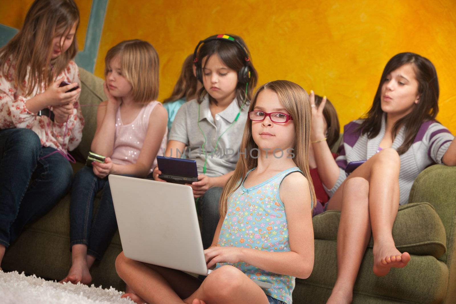 Little girl using laptop while her friends are busy playing on video game consoles