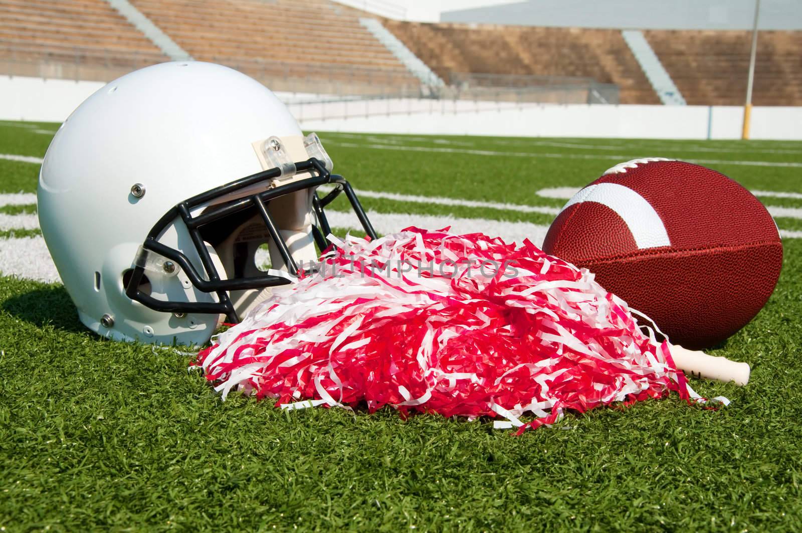 American football, helmet, and pom poms on field in stadium.