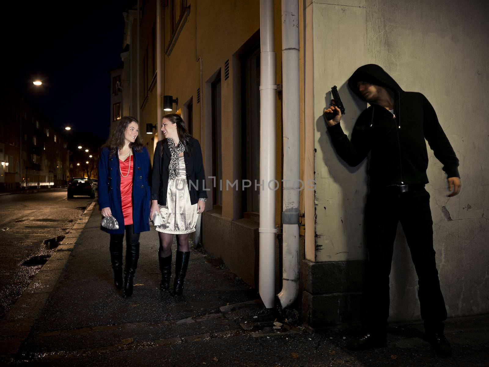 Hooded man stalking two women behind a corner holding a gun