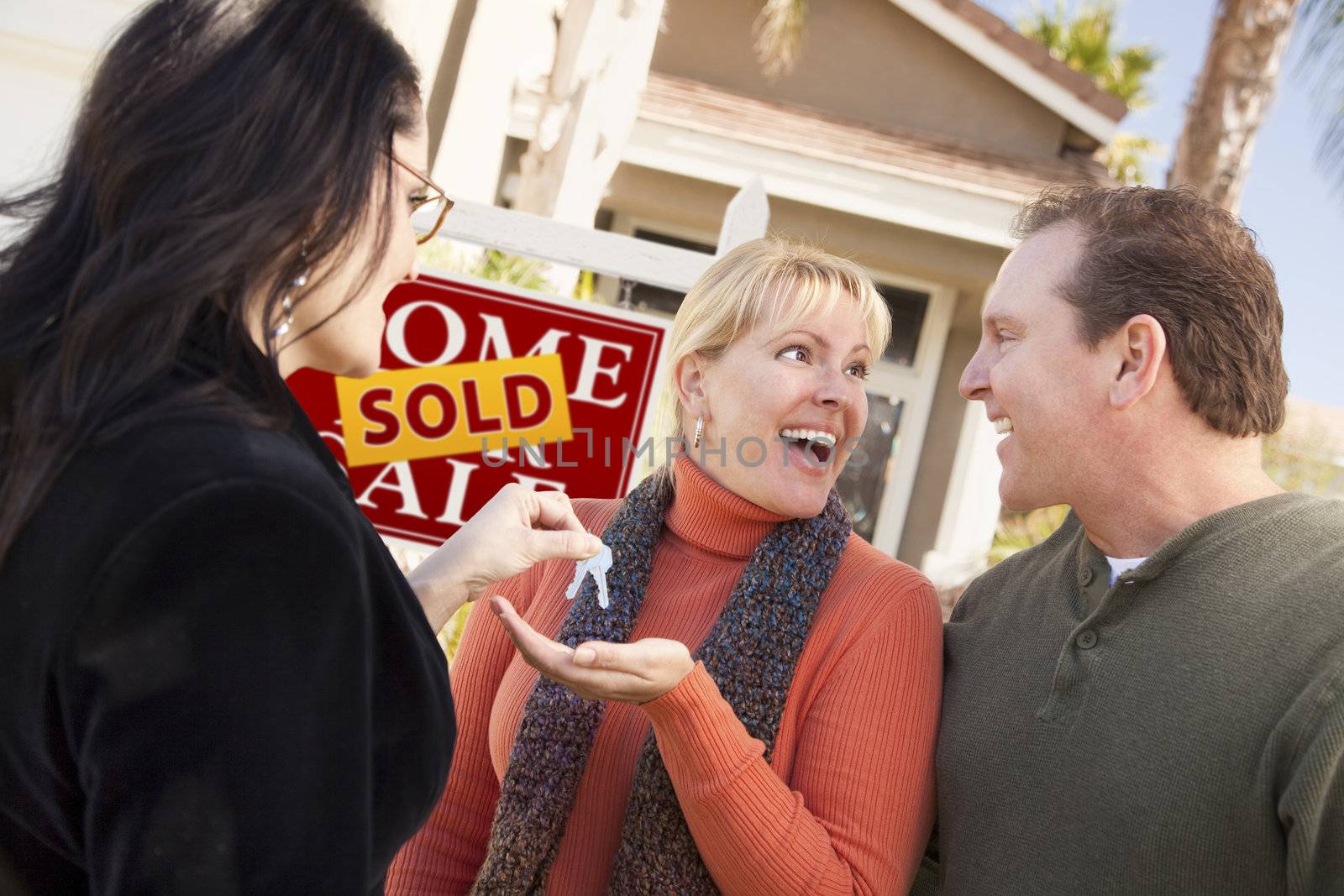 Hispanic Female Real Estate Agent Handing Over New House Keys to Excited Couple.