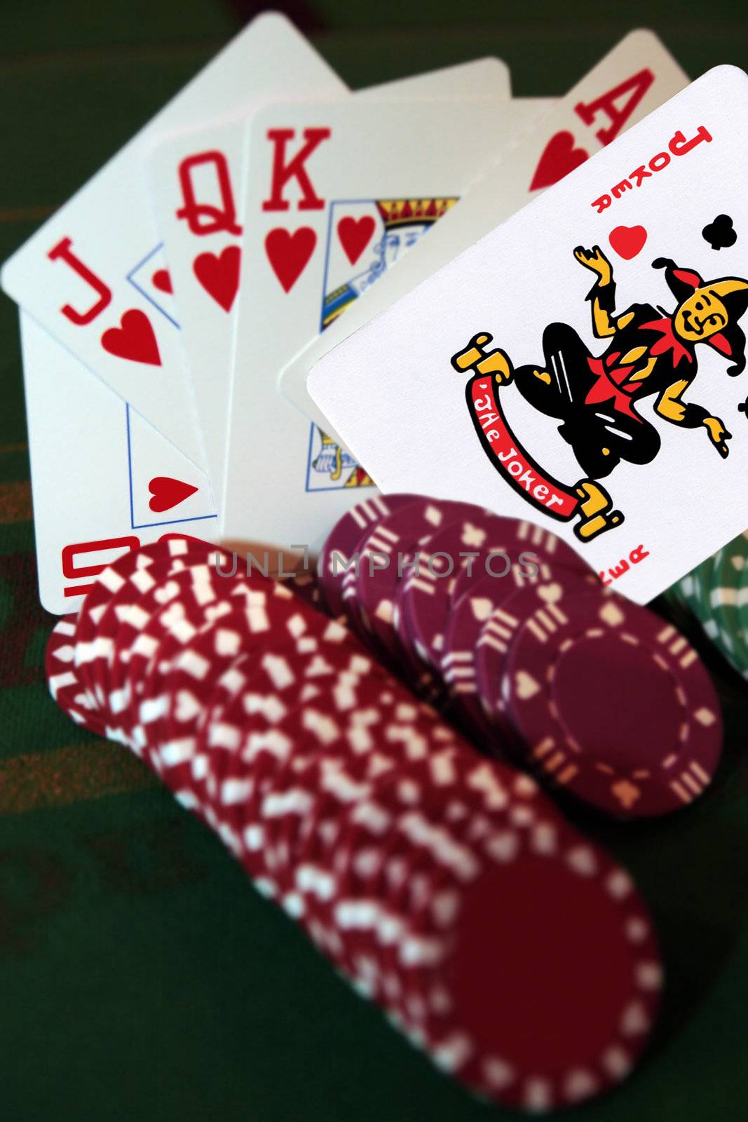 green casino table with chips and a hand of a royal flush in a poker game and a joker in the pack