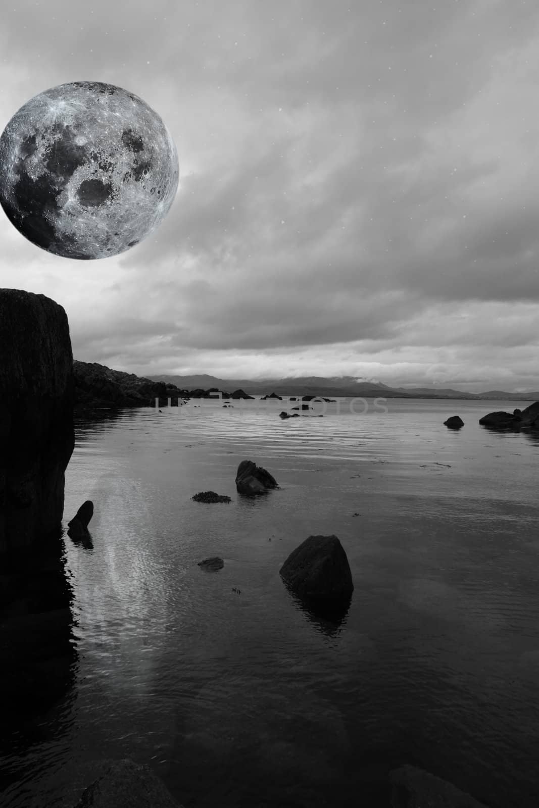 black and white night scenic view in kerry ireland of rocks and sea with mountains against a beautiful blue cloudy sky