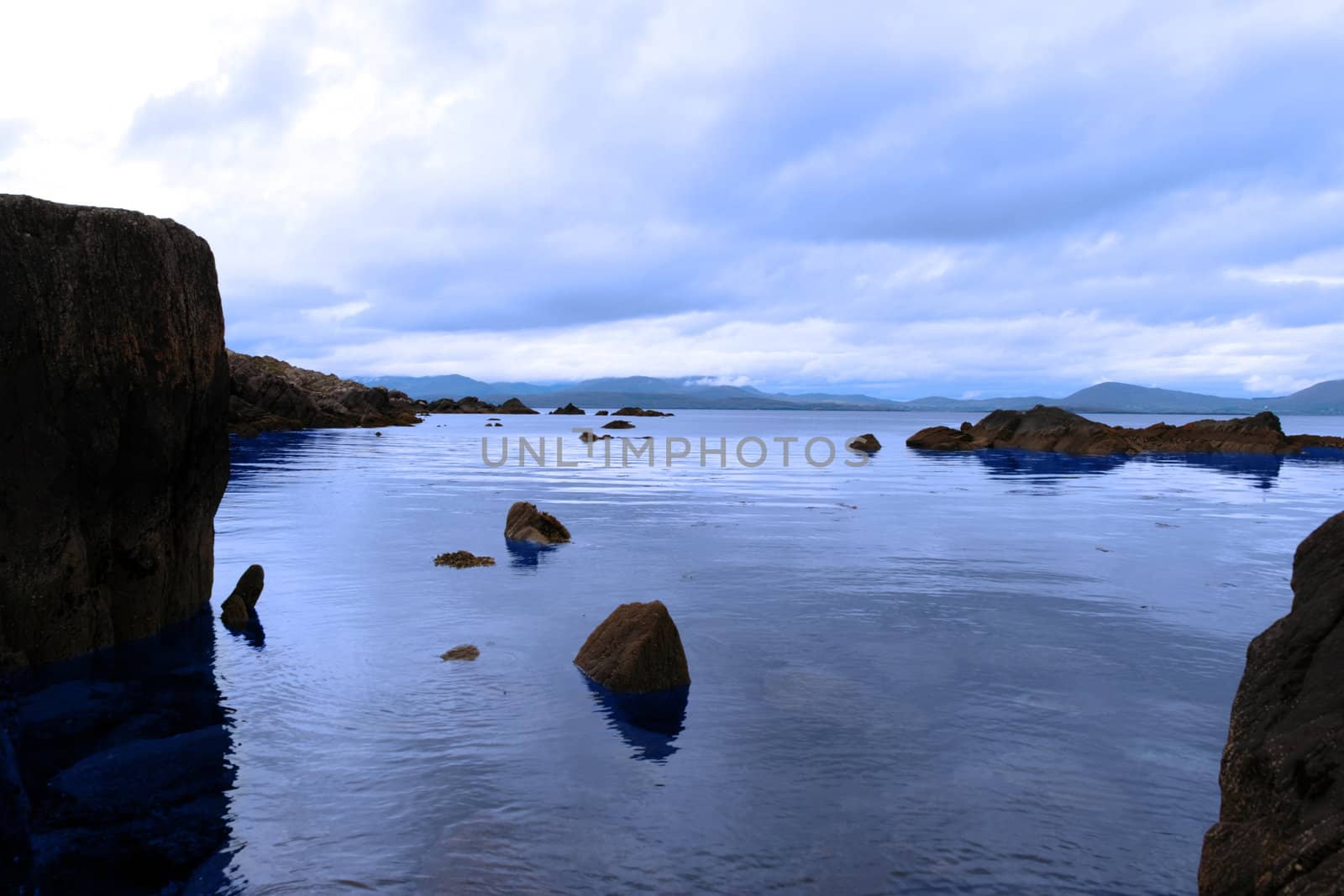 scenic view in kerry ireland of rocks and sea with mountains against a beautiful blue cloudy sky