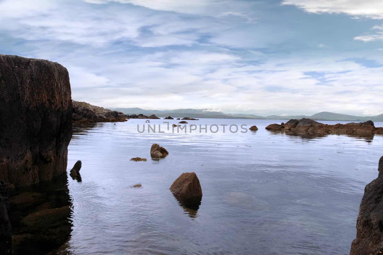 scenic view in kerry ireland of rocks and sea with mountains against a beautiful blue cloudy sky