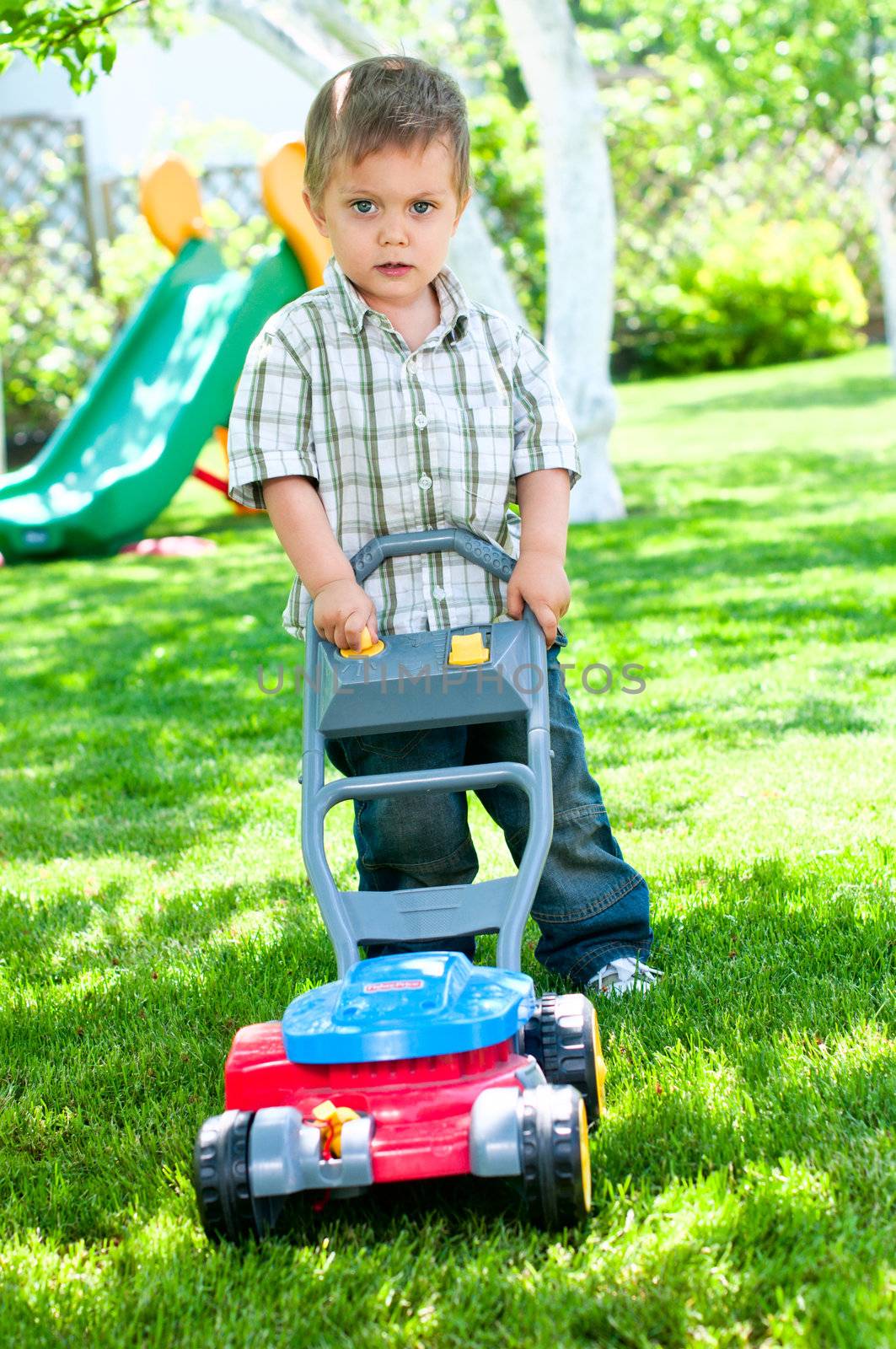 Happy little boy with lawn mower in the garden