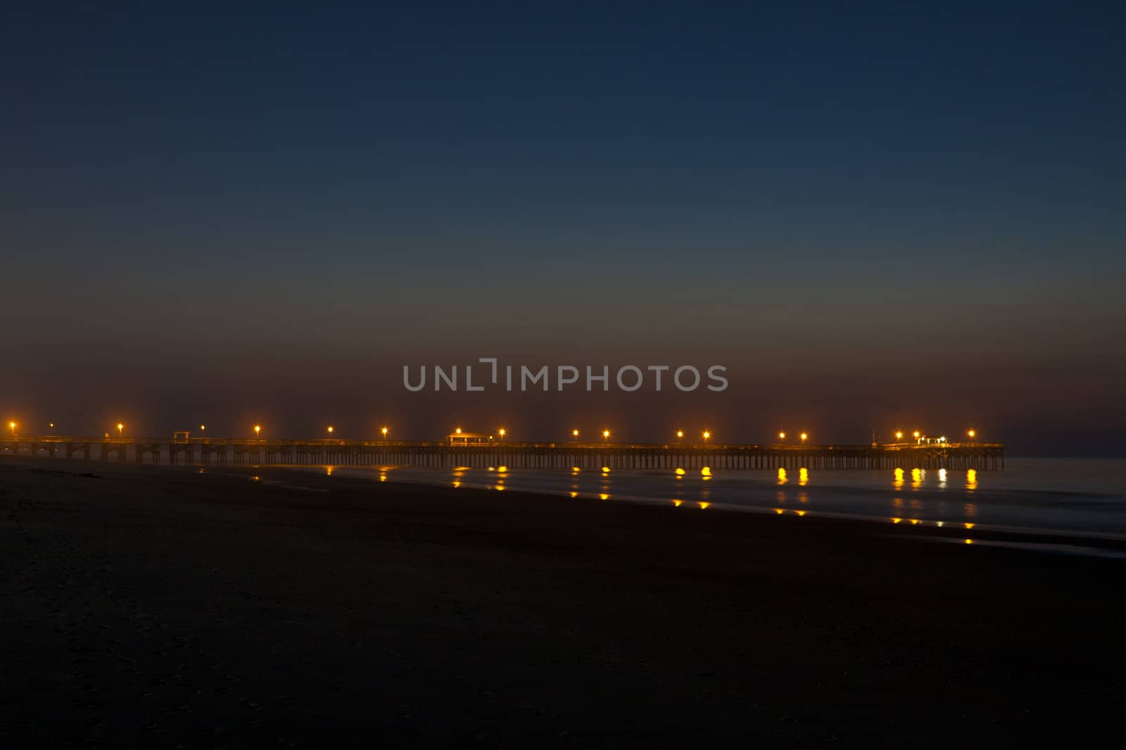 wonderful shot of the sun rising over a pier at an ocean beach