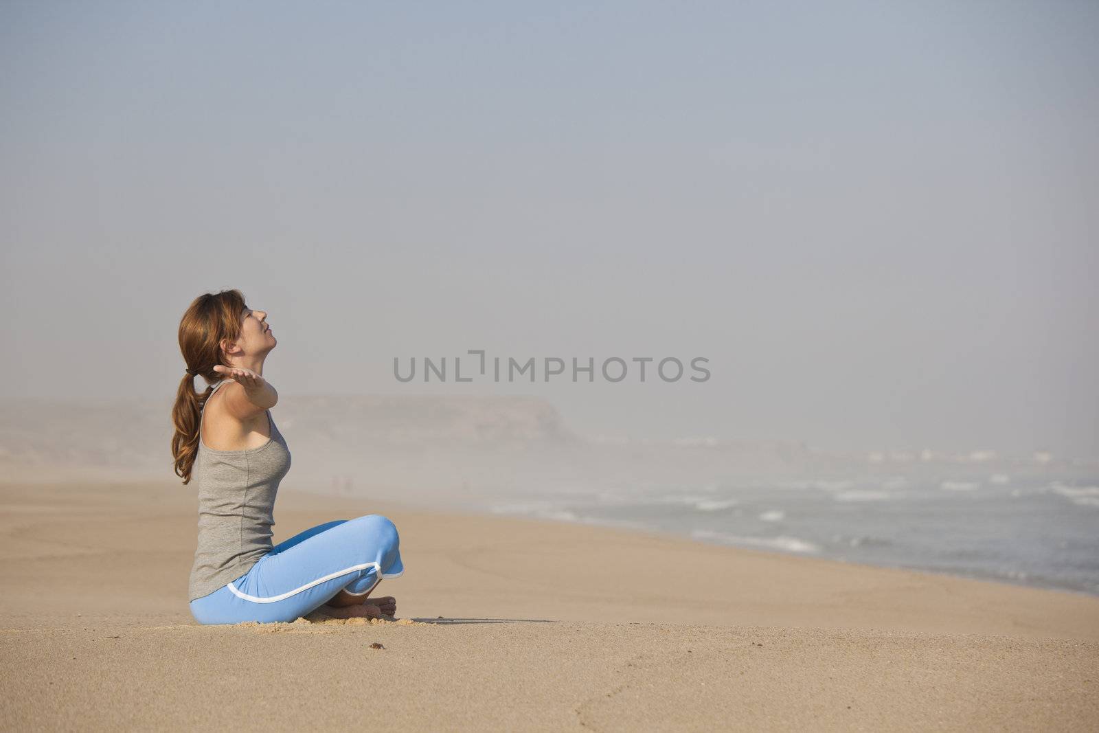 Beautiful young woman on the beach doing yoga exercises