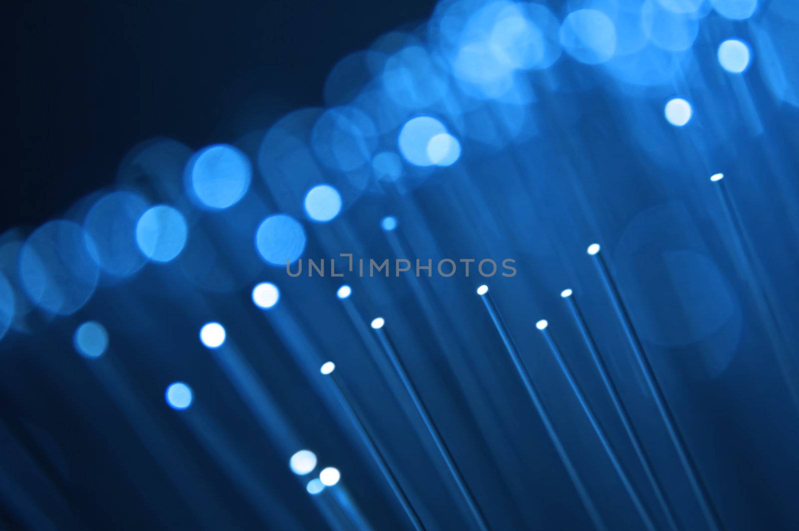 Close up on the ends of many illuminated blue fiber optic strands with black background. Focus on foreground.