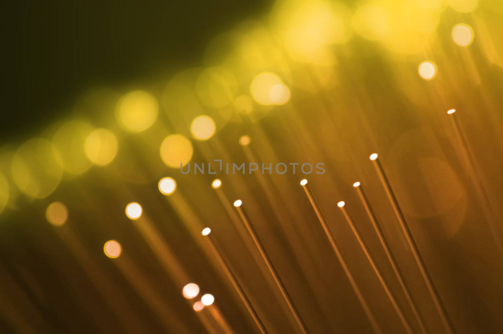 Close up on the ends of many illuminated golden fiber optic strands with dark background. Focus on foreground.
