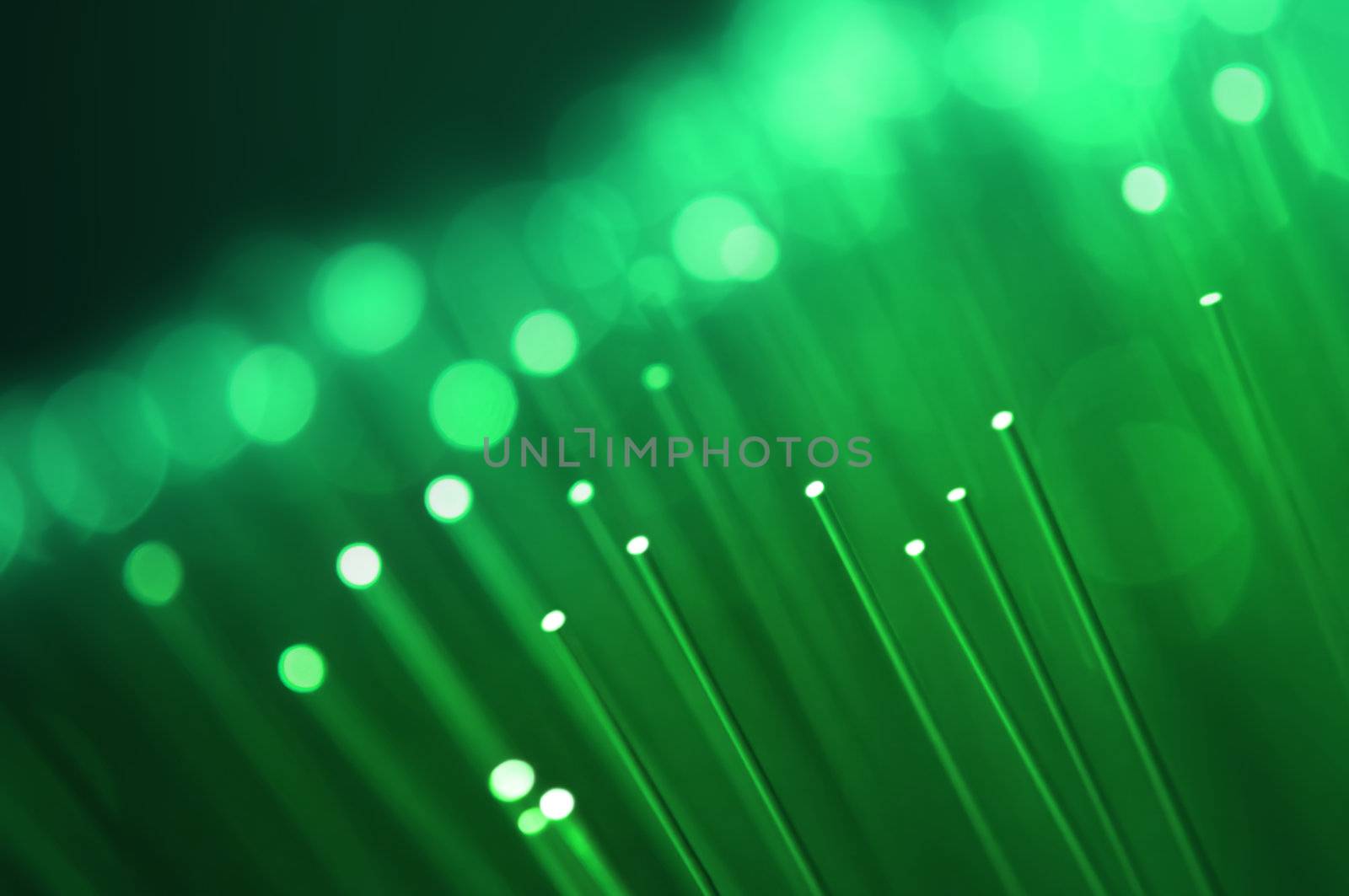 Close up on the ends of many illuminated green fiber optic strands with black background. Focus on foreground.