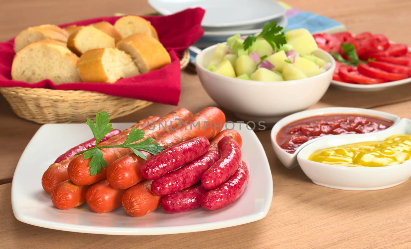 Two types of sausages with ketchup, mustard, potato salad, baguette and tomato slices (Selective Focus, Focus on the front of the sausages)