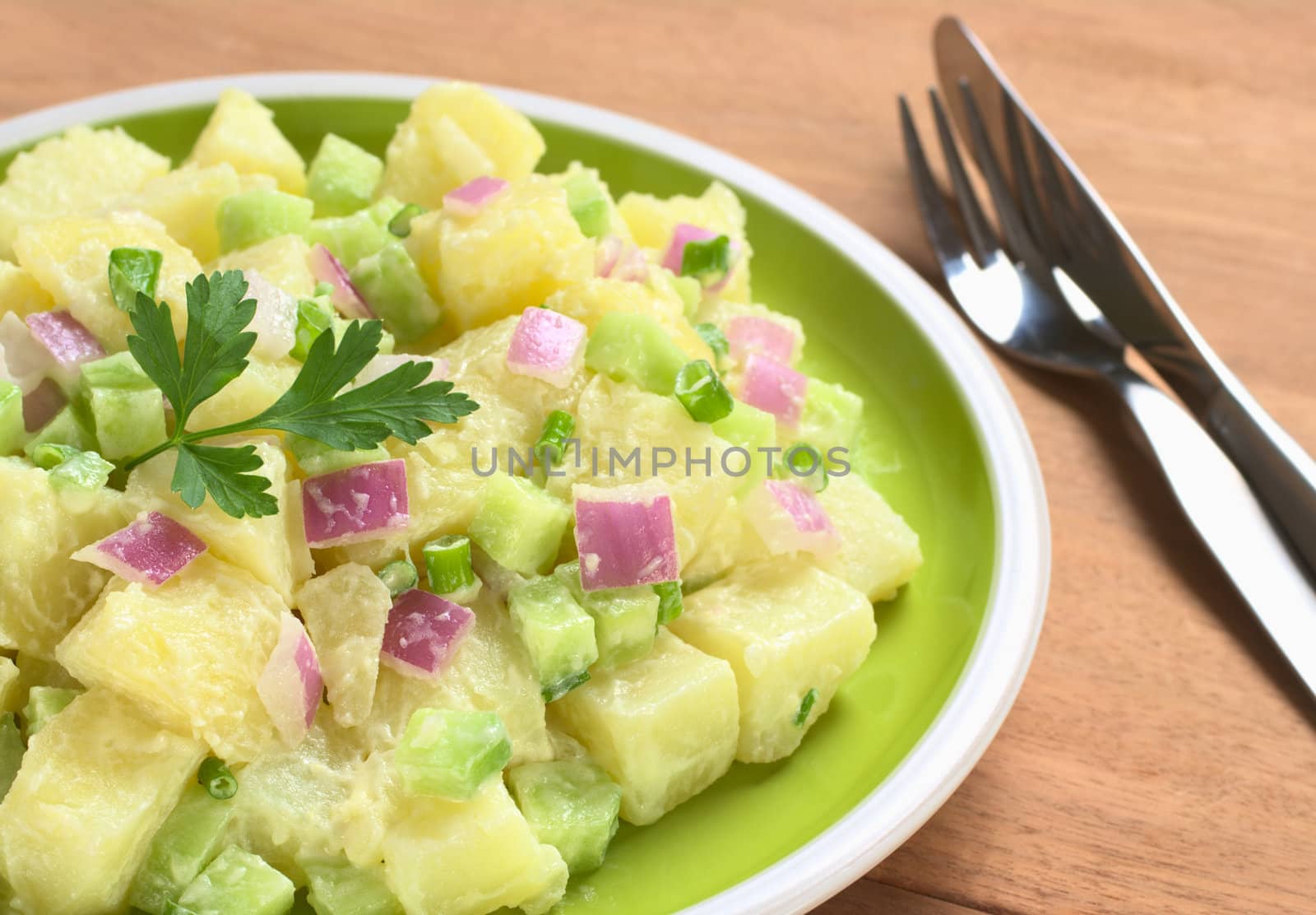 Potato salad with green and red onions and cucumber with a mayonnaise-cream dressing garnished with a parsley leaf (Selective Focus, Focus on the front of the salad)  