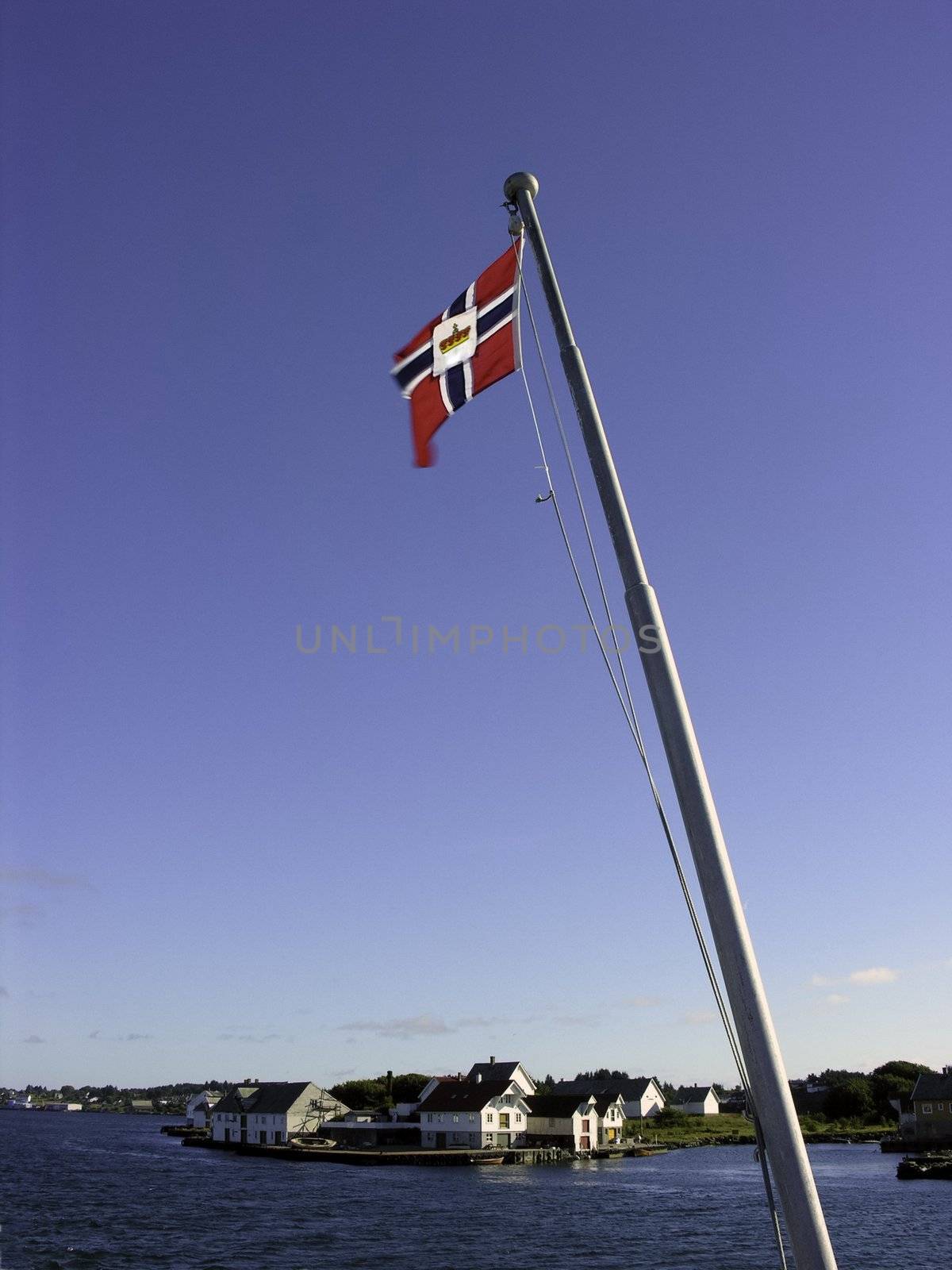 Norway flagpole in blue sky with a village in background