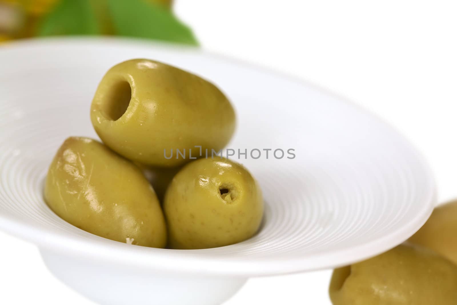 Green olives in a small bowl with olives lying beside (Very Shallow Depth of Field, Focus on the front close to the opening of the top olive)