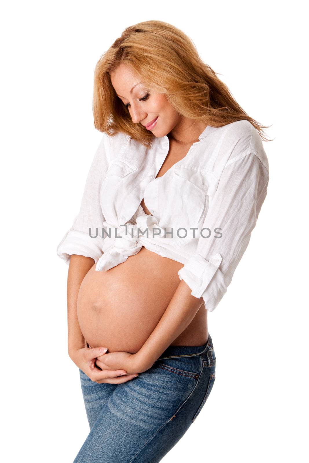 Beautiful new happy mother in late pregnancy wearing fashion jeans and white, looking at tummy holding belly, isolated.