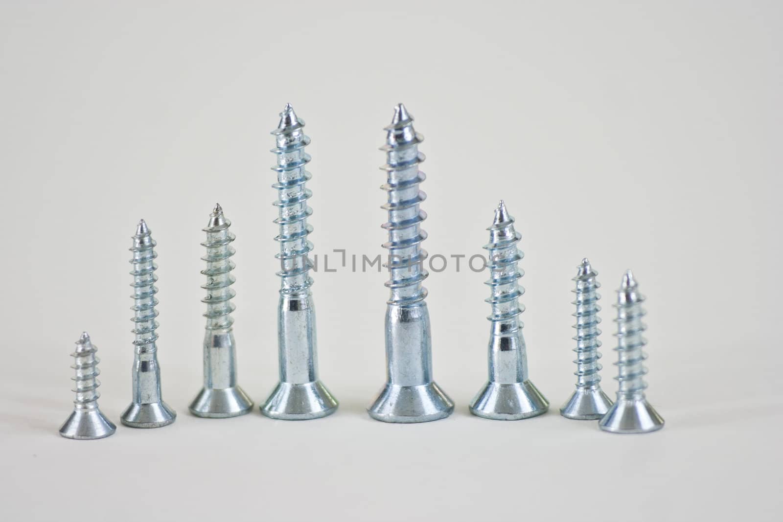 Different sizes of screws lined up in desending order on a white background.
