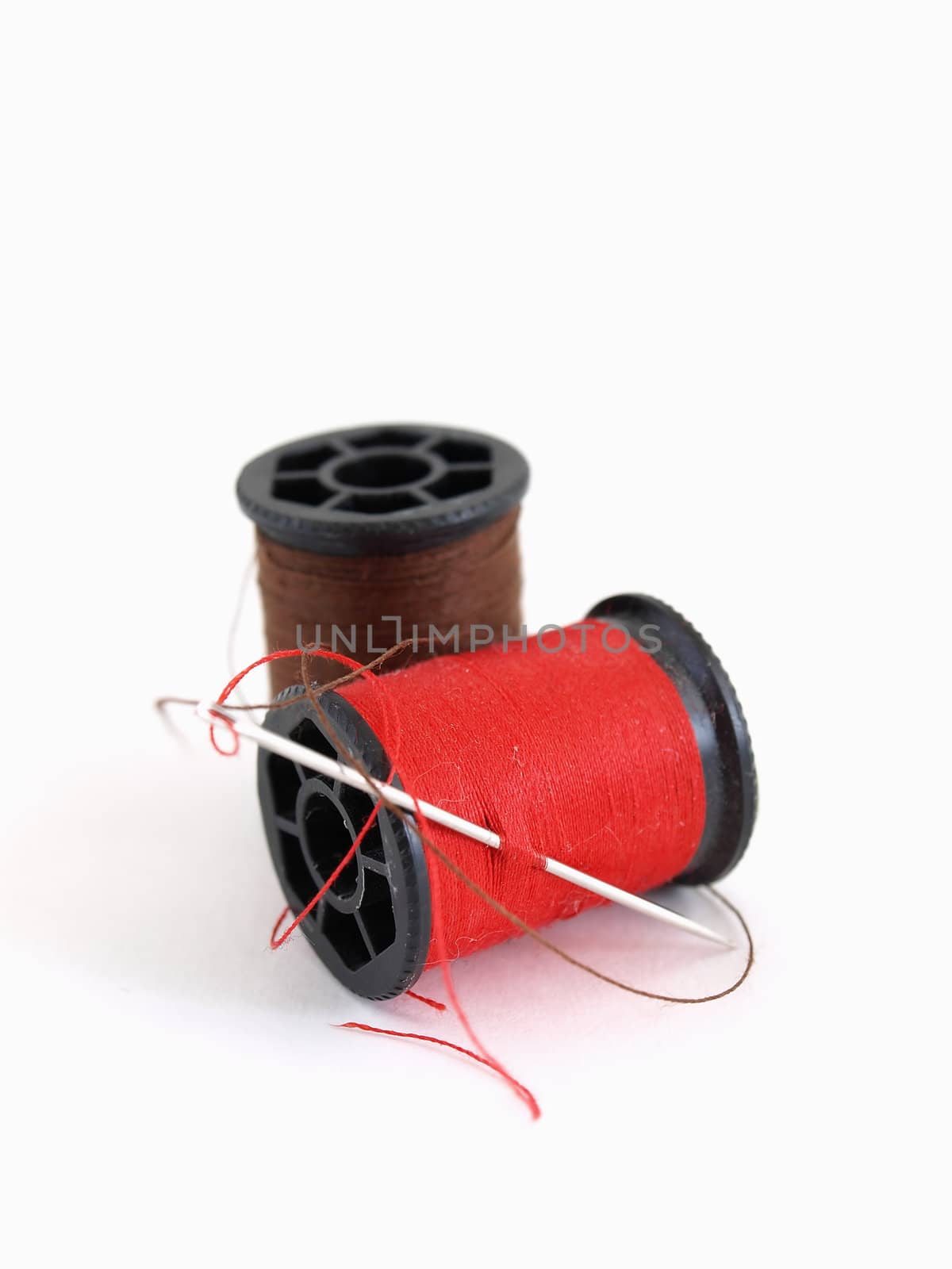 Two spools of thread and a needle, isolated on a white background.