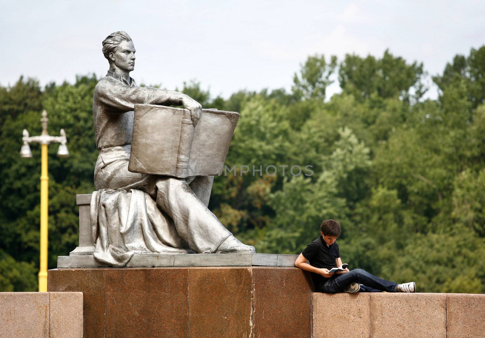 The student reads the book near to a statue
