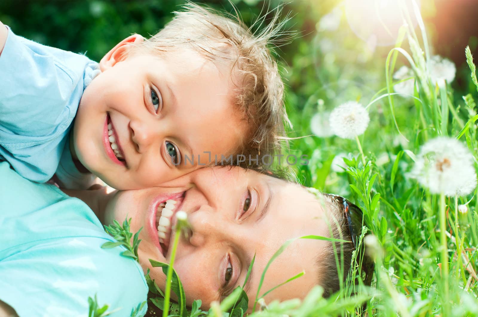 Cute 2 years old boy with mother lying in the grass at sunny summer day
