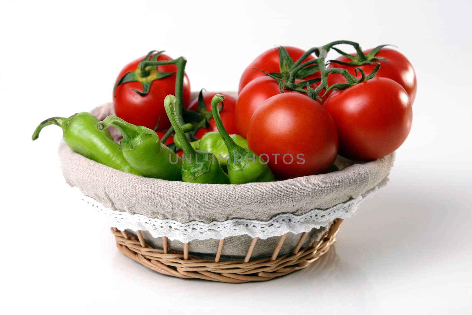 Red tomatoes and green peperoni in basket on white background