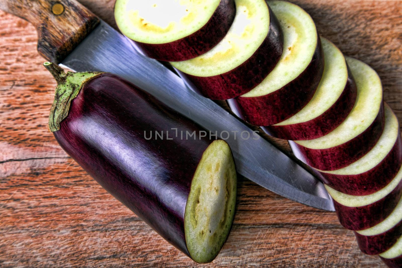 Eggplant sliced on wood cutter with a knife