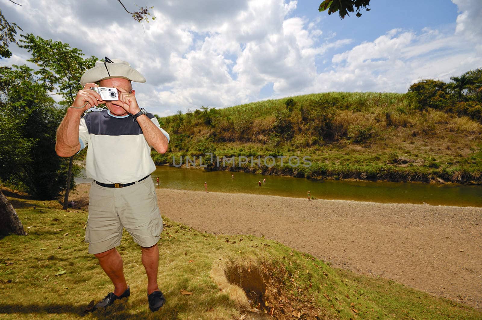 A turist is standing in green nature. The man is a senior and is holding a camera. Dominican Republic.