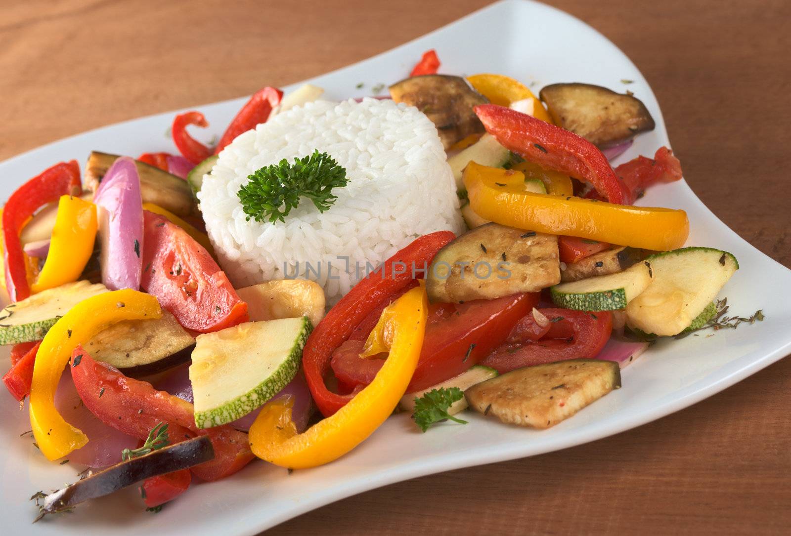 Ratatouille of zucchini, eggplant, tomato, bell pepper and onion with cooked rice and parsley on top (Selective Focus, Focus on the front of the rice, the parsley on top and the vegetable around)