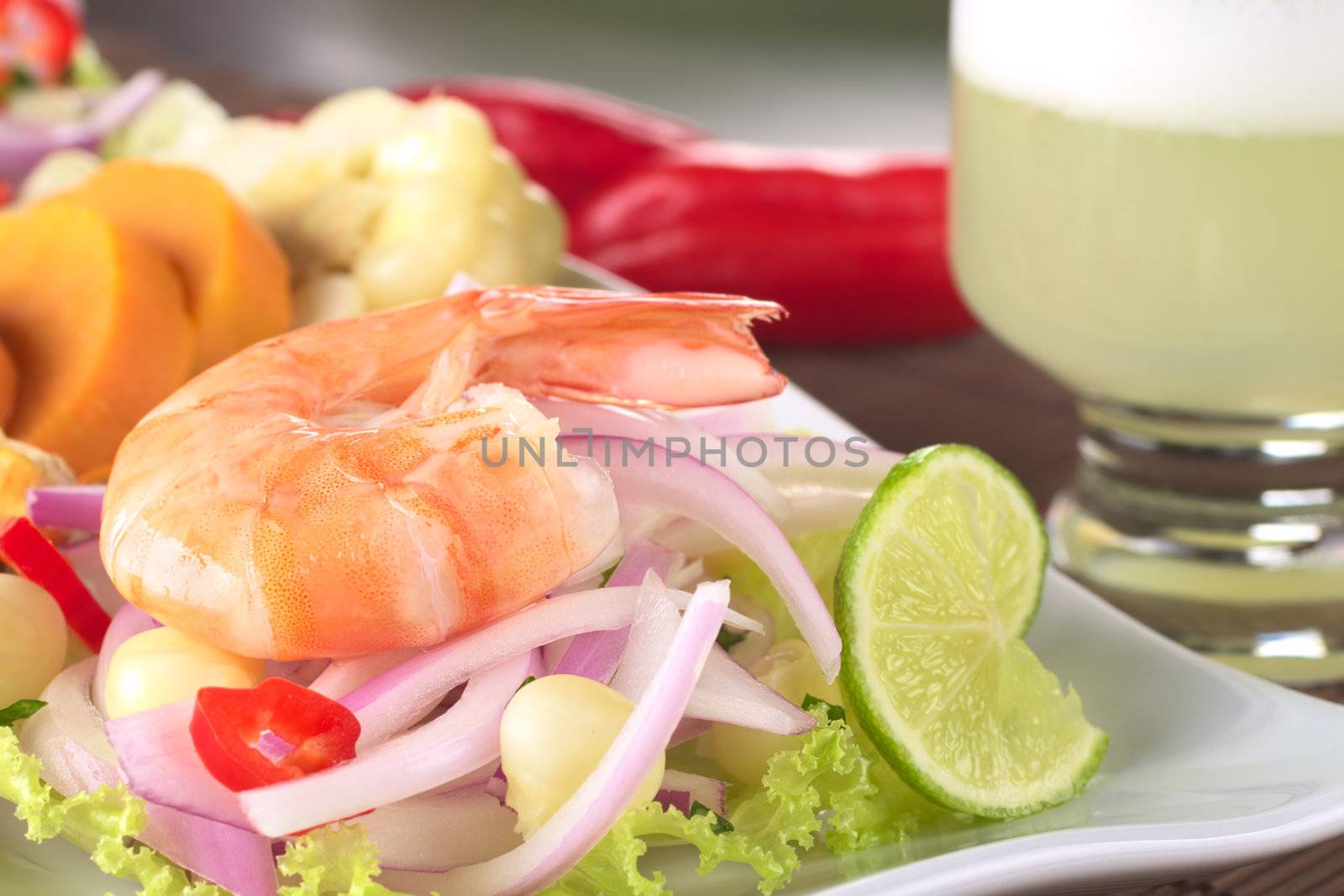 Peruvian Prawn Ceviche: King prawn on red onions and lettuce with corn grains, lime slices and sweet potato in the back and the Peruvian cocktail called Pisco Sour on the side (Selective Focus, Focus on the front of the prawn)  