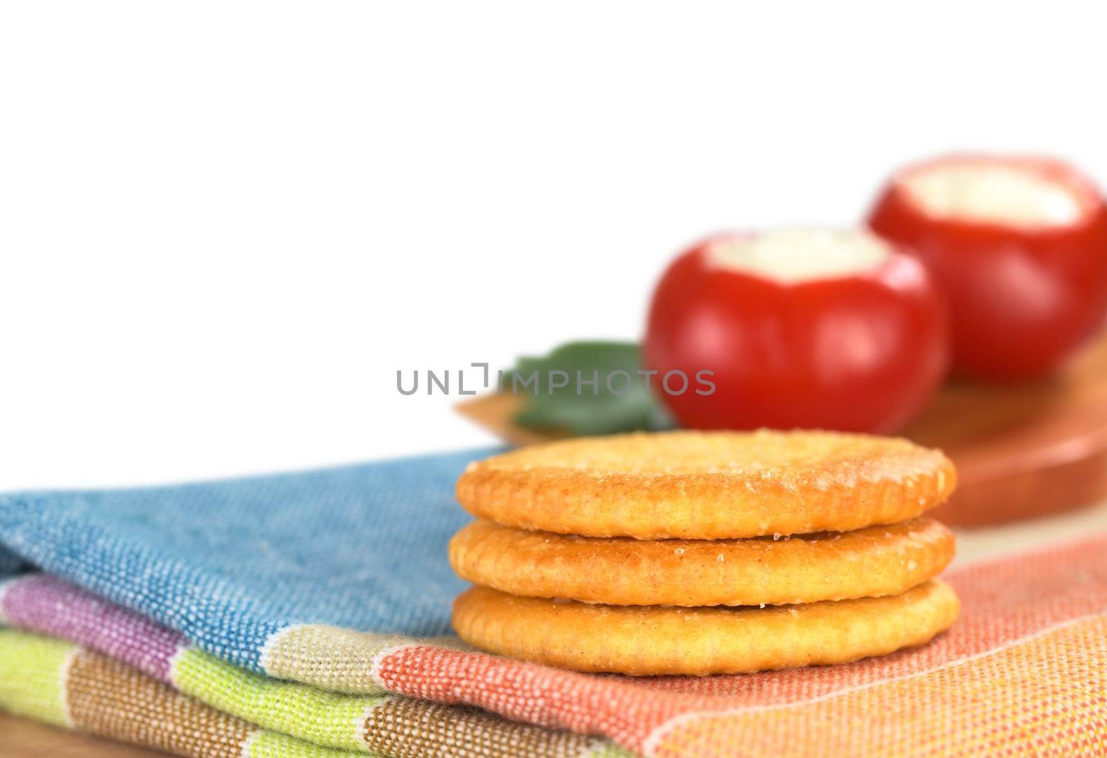 A pile of salty crackers on textile with round red pepper in the back (Very Shallow Depth of Field, Focus on the front of the crackers)