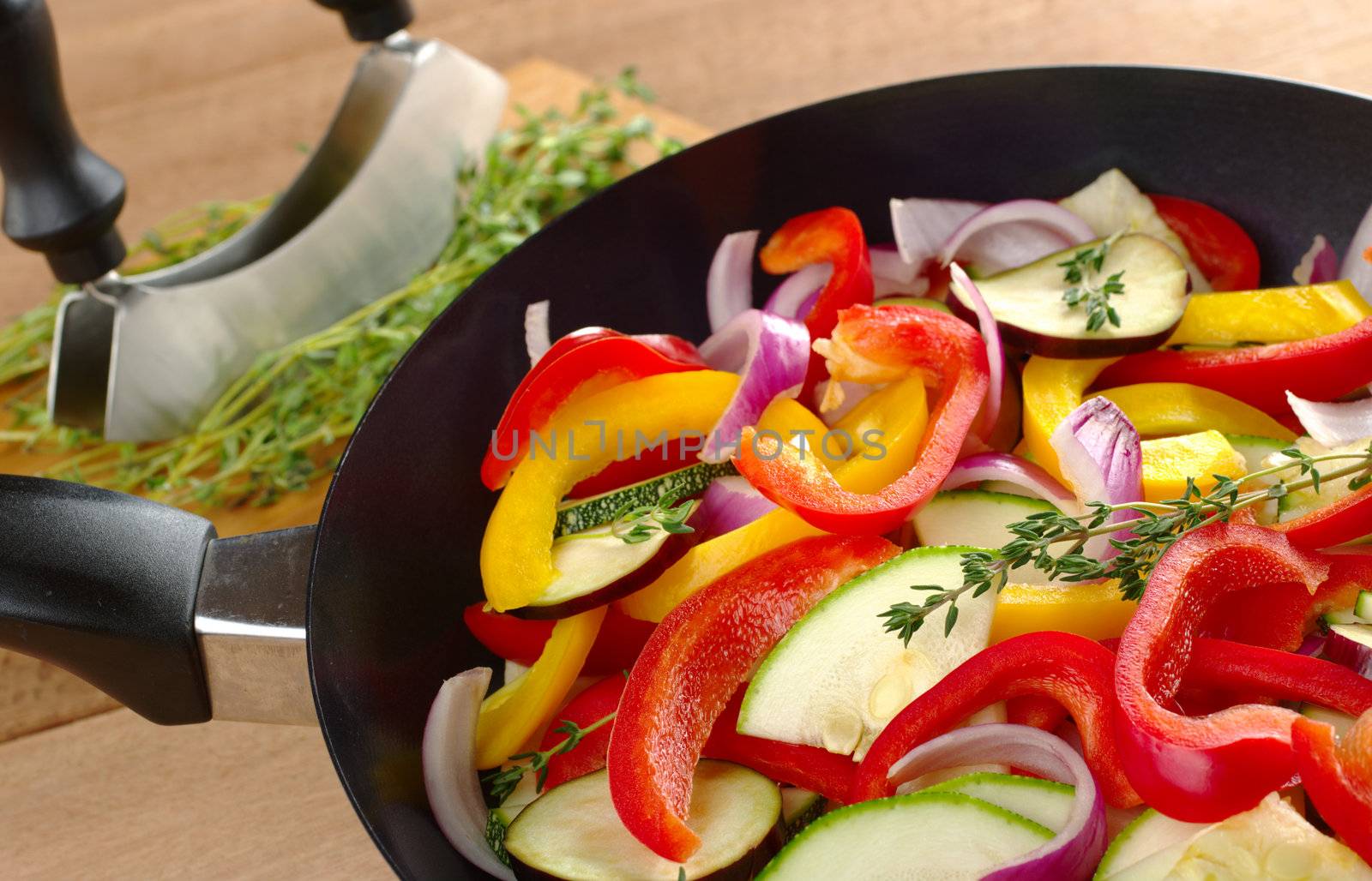 The raw ingredients (zucchini, bell pepper, onion, eggplant) of ratatouille in a frying pan with thyme on top and in the background (Selective Focus, Focus on the thyme sprig in the frying pan)