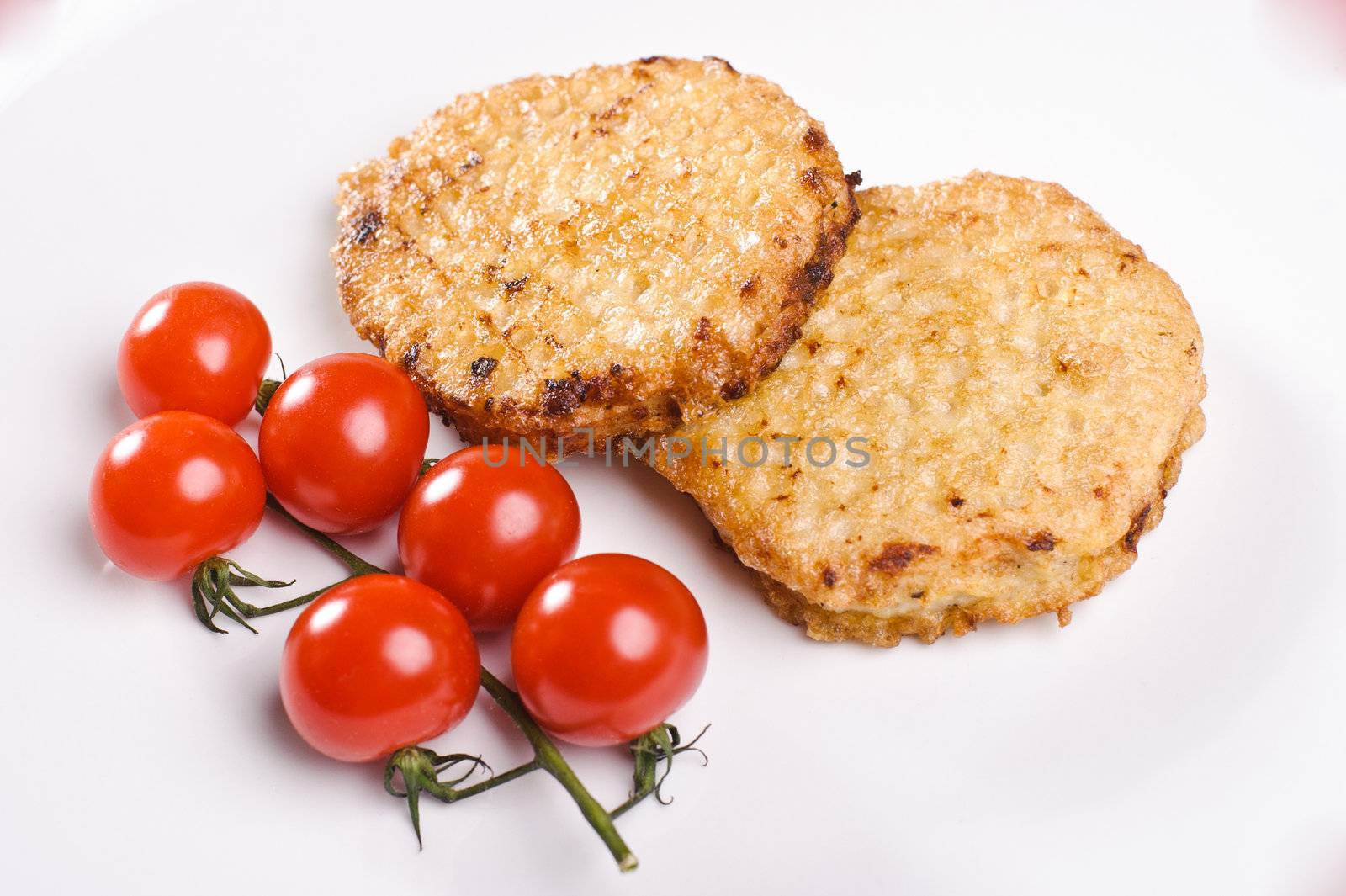 Two cutlets with branch of small tomatos on white plate