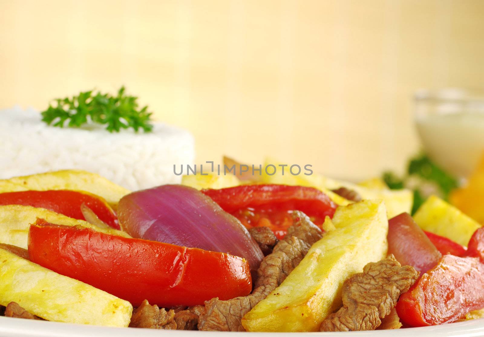 A typical Peruvian dish called Lomo Saltado which is made of beef, onions, tomatoes and is accompanied by fried potatoes and rice (Selective Focus, Focus on the front of the dish)