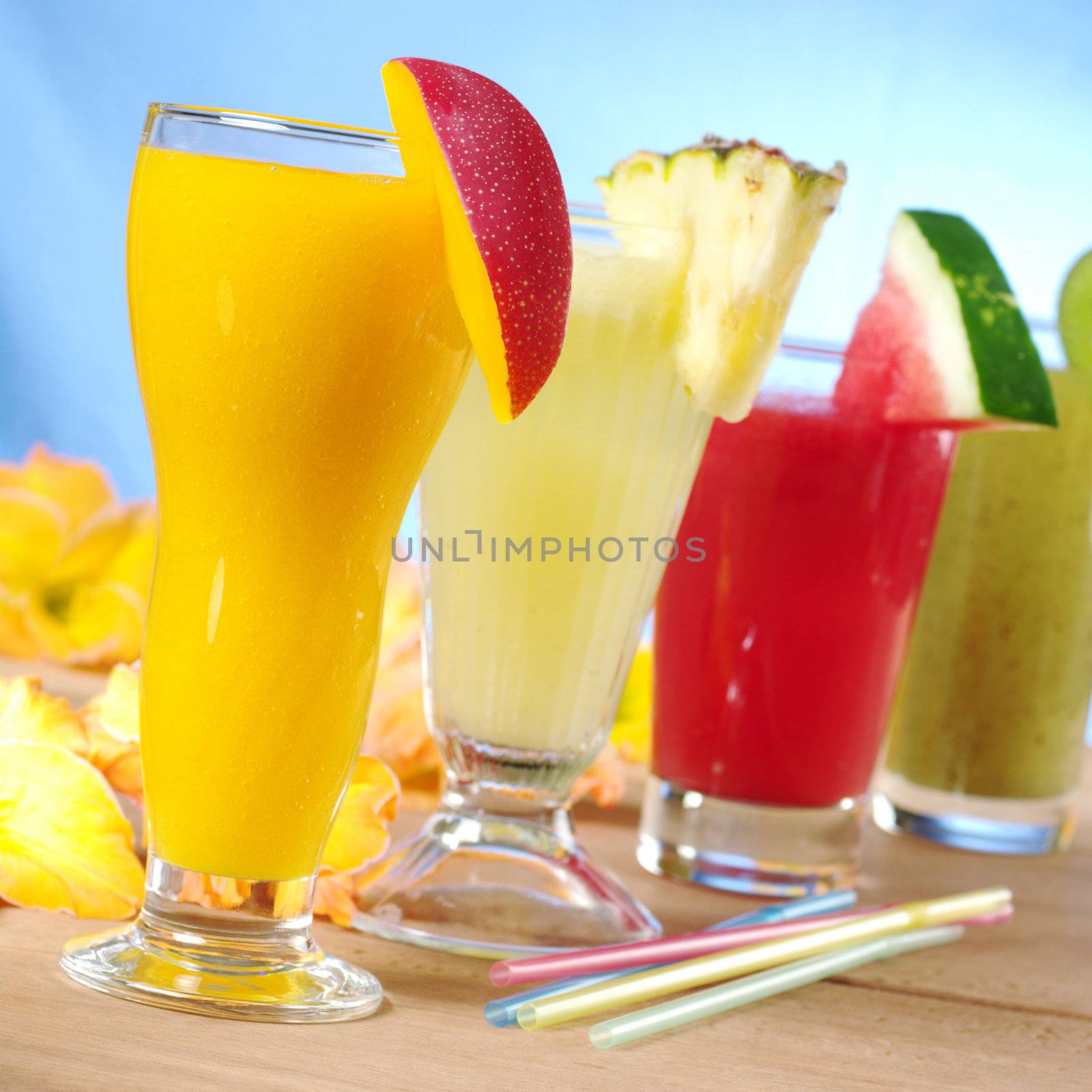 Mango, pineapple, watermelon and kiwi smoothie with drinking straws on wood (Selective Focus, Focus on the mango smoothie in the front)