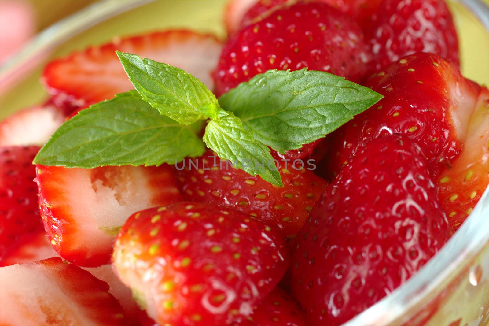 Mint leaf garnishing fresh half strawberries in a glass bowl (Selective Focus, Focus on the mint leaf)