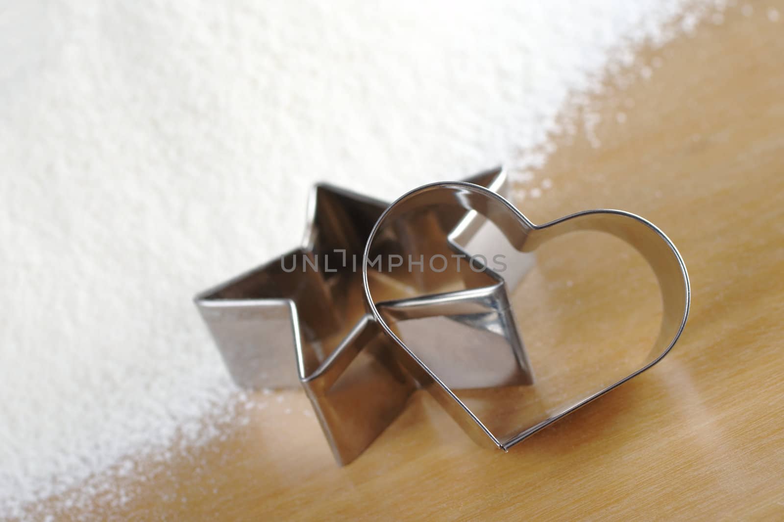 Heart and star shaped cookie cutters with flour in the background (Selective Focus, Focus on the heart cookie cutter)