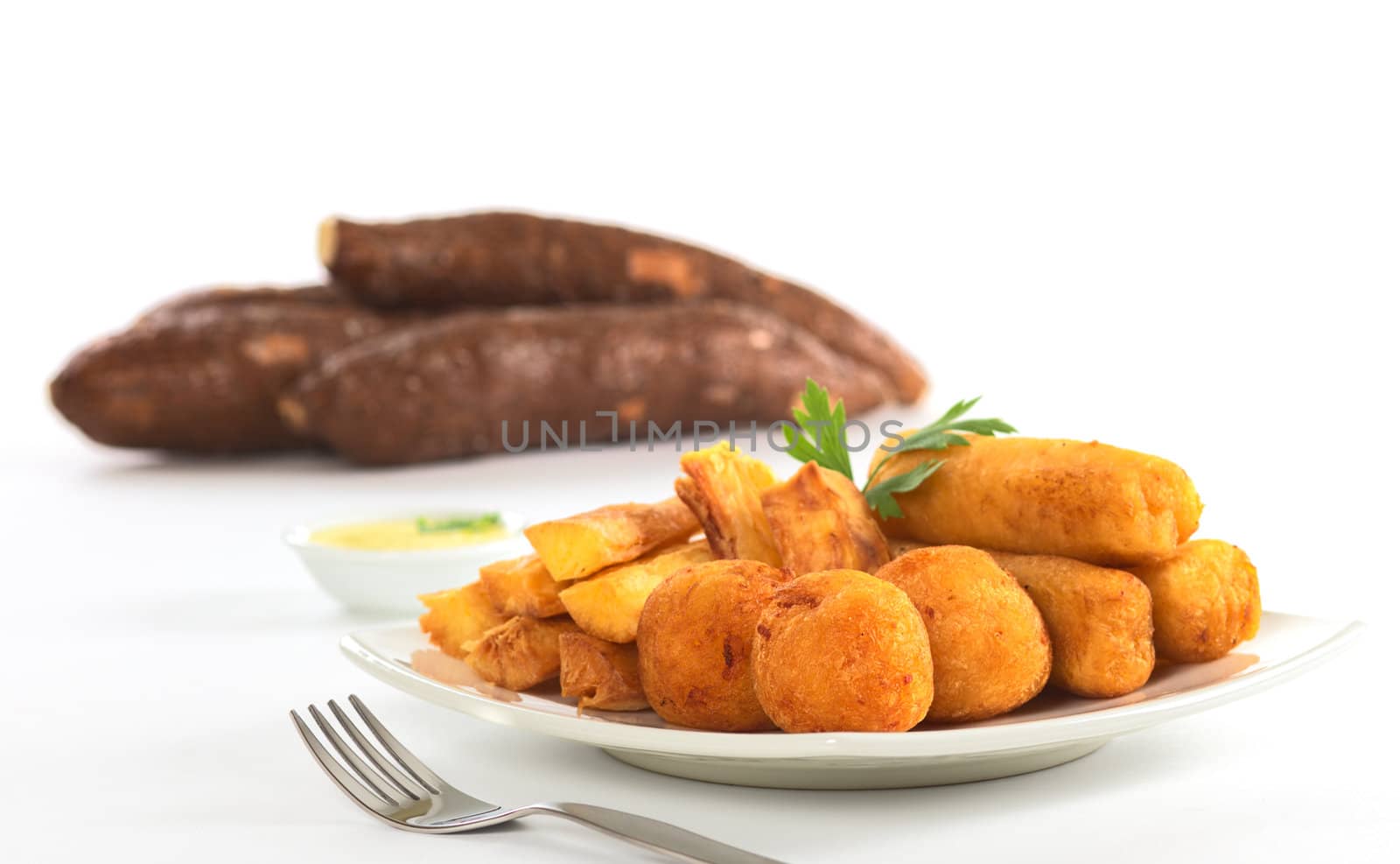 Filled fried balls and sticks out of manioc with a dip and some manioc roots in the back (Selective Focus, Focus on the manioc balls)