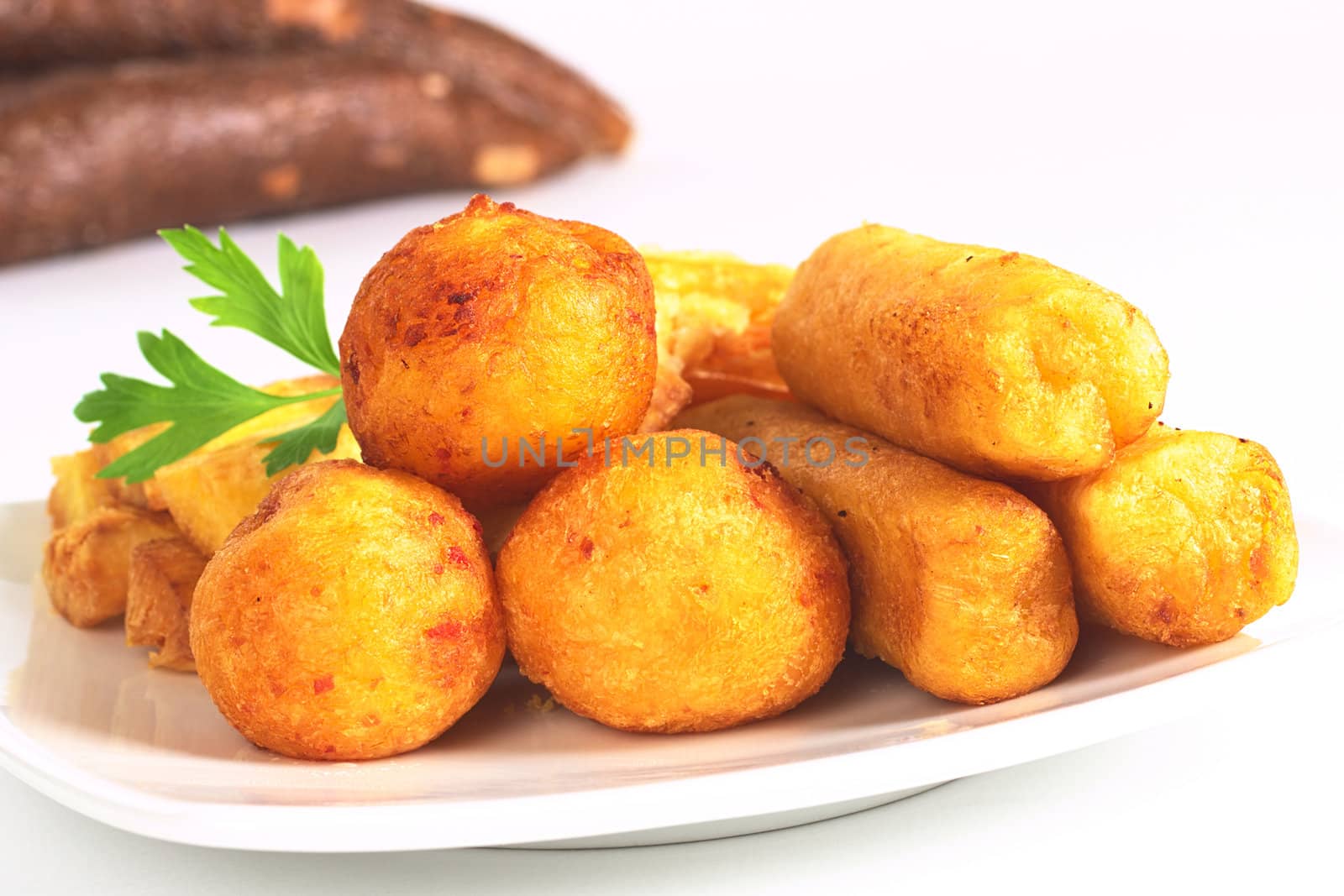Filled fried balls and sticks out of manioc garnished with parsley and with manioc roots in the back (Selective Focus, Focus on the front)