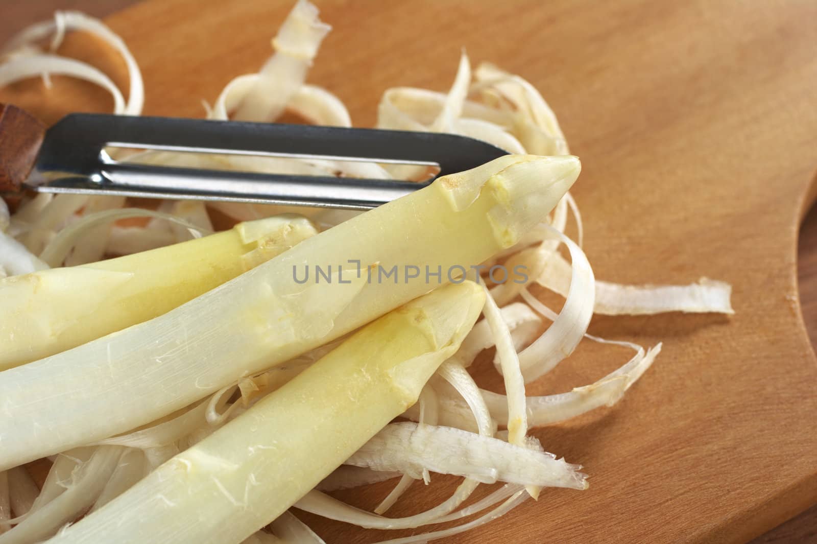 Peeling white asparagus on a wooden cutting board (Selective Focus, Focus on the head of the asparagus on the top) 