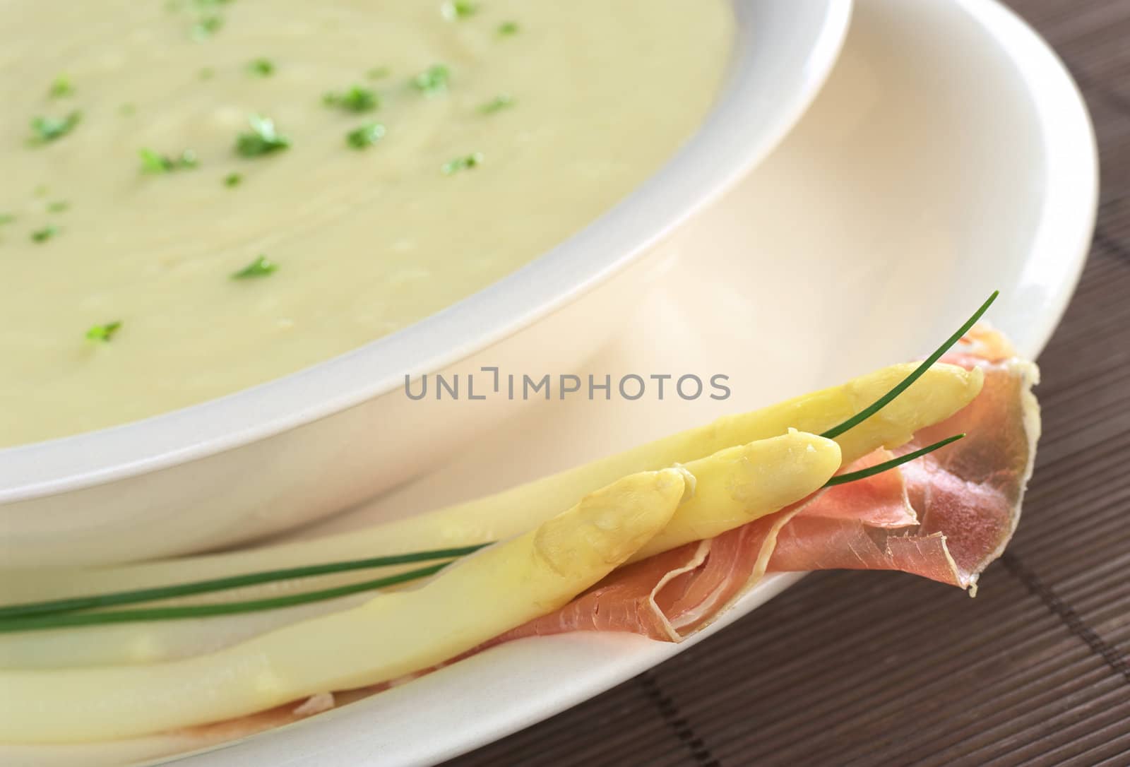 Cream of white asparagus garnished with parsley and white asparagus, ham and chives on the rim (Selective Focus, Focus on the front of the asparagus heads and ham) 