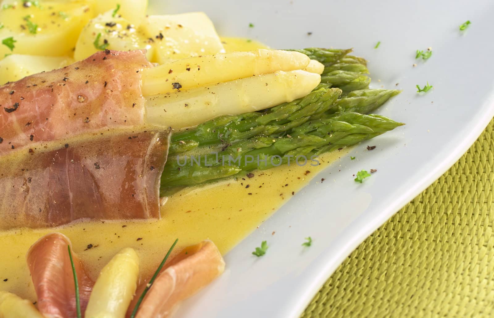 White and green asparagus wrapped in thin ham slices with Hollandaise sauce on top garnished with black pepper and parsley (Selective Focus, Focus on the front of the green and white asparagus and ham) 