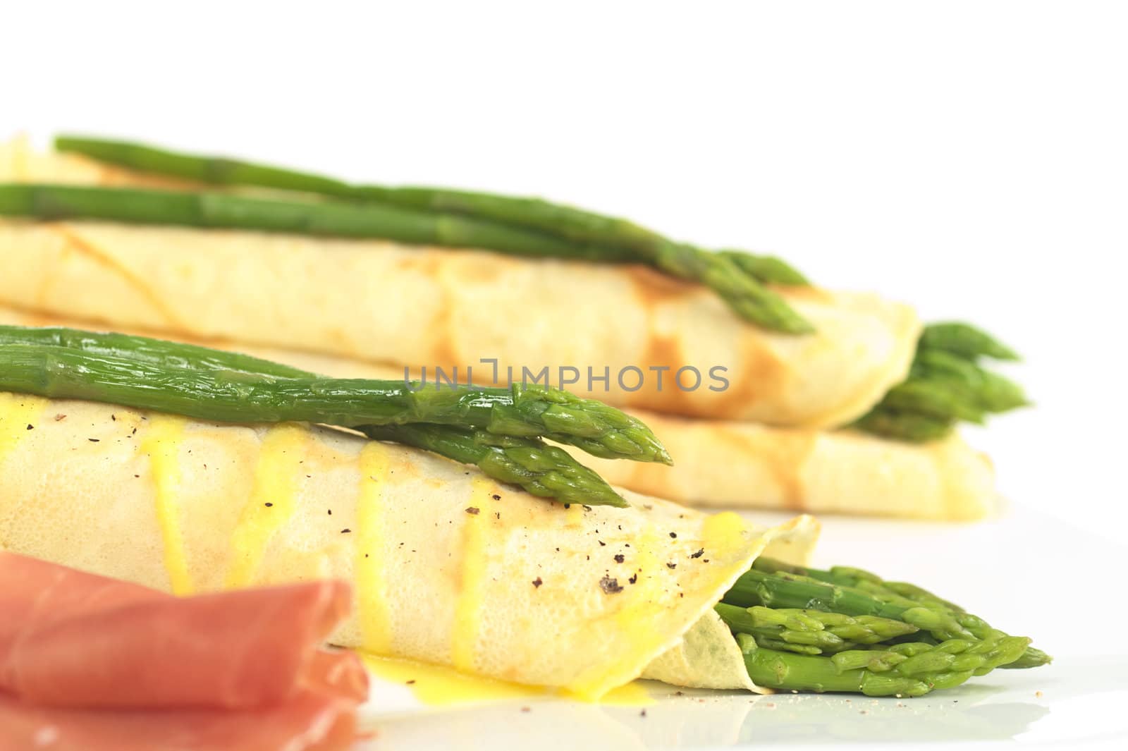 Green asparagus wrapped in crepes with Hollandaise sauce and green asparagus as garnish on top (Selective Focus, Focus on the asparagus in the front)