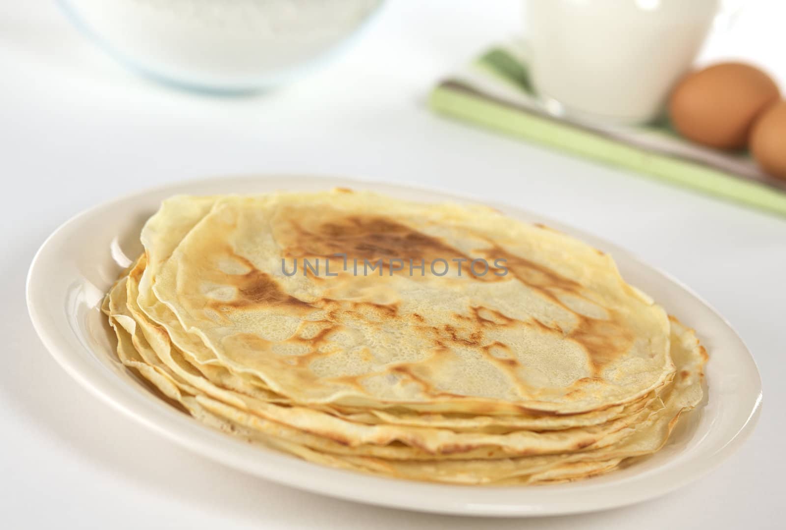 Crepes (thin pancakes) with ingredients for the batter in the back (Selective Focus, Focus one third from front on the surface of the pancake)