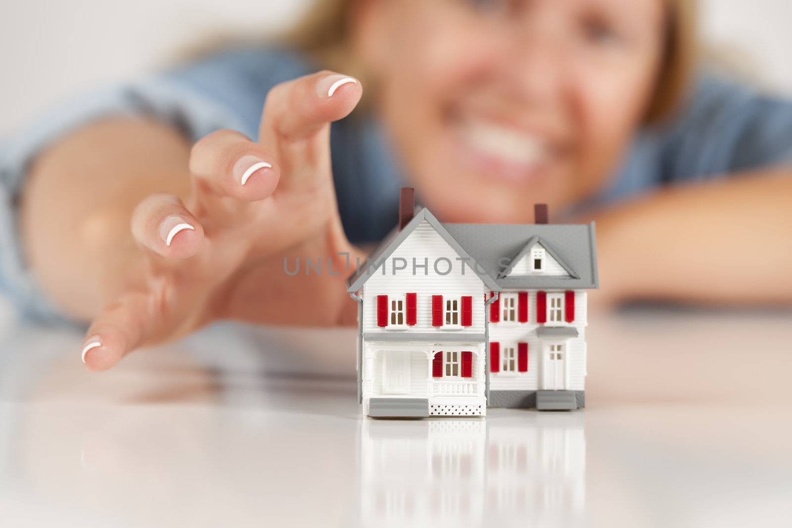 Smiling Woman Reaching for Model House on a White Surface.