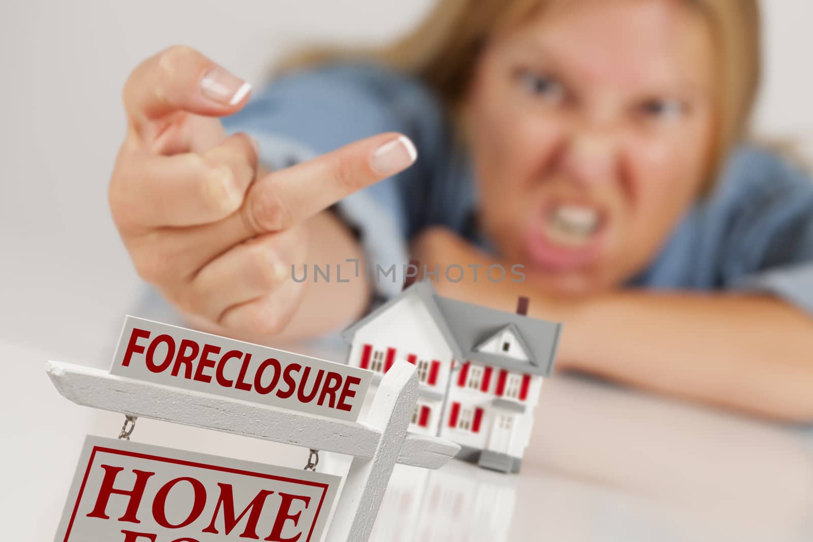 Angry Woman Flipping The Bird Behind Model Home and Foreclosure Real Estate Sign in Front.