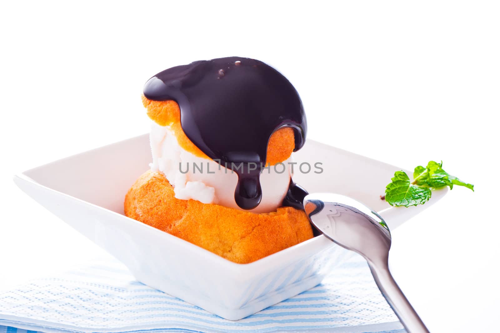 Profiterole in a small bowl with ice cream chocolate sauce and mint leaf on a white backgound