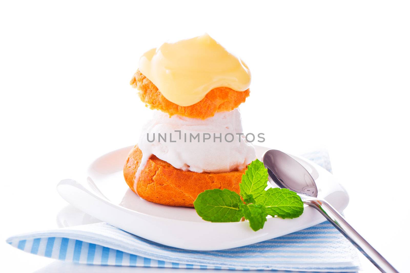 Profiterole in a small plate with ice cream vanilla sauce and mint leaf on a white backgound