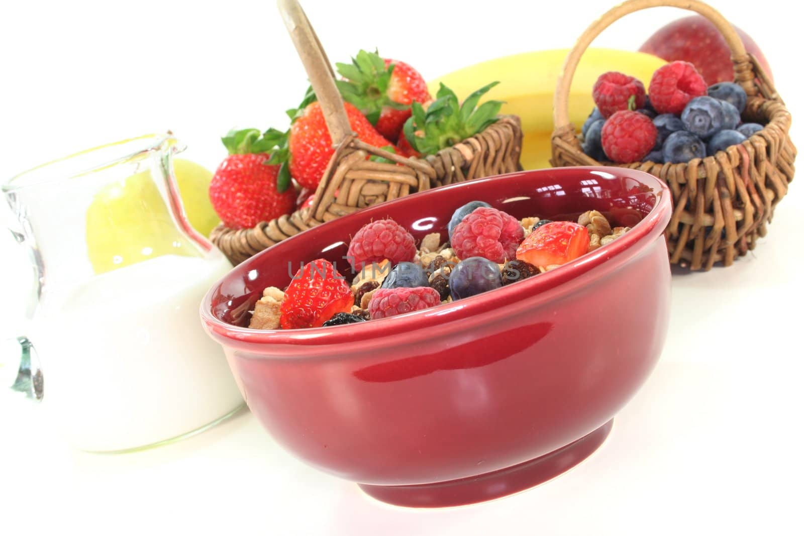 Cereal bowl of fresh fruit, nuts and milk before a white background